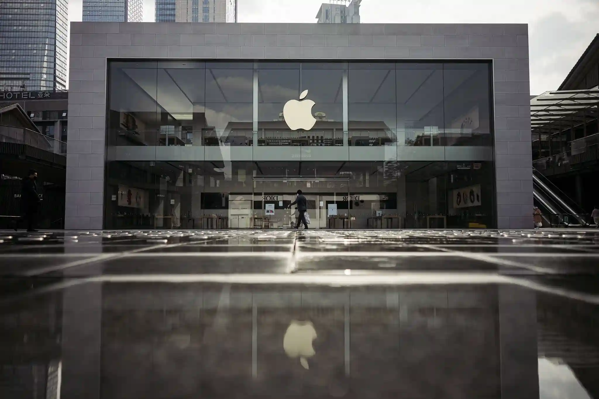 Apple Store glass facade with large Apple logo reflected on wet pavement in a modern city setting