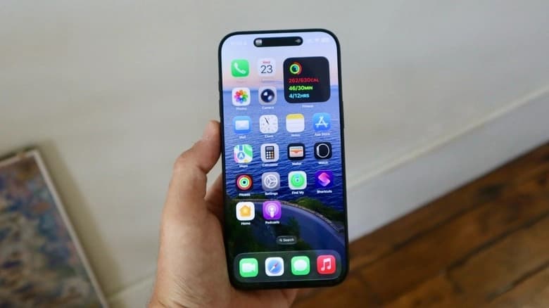 Hand holding an iPhone showing the iOS home screen with apps and widgets.