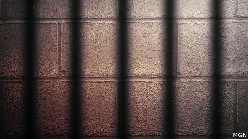 Empty prison cell with shadowed bars on the wall.