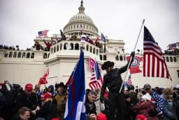 Supporters storm the U.S. Capitol during the January 6th riot with American flags flying.