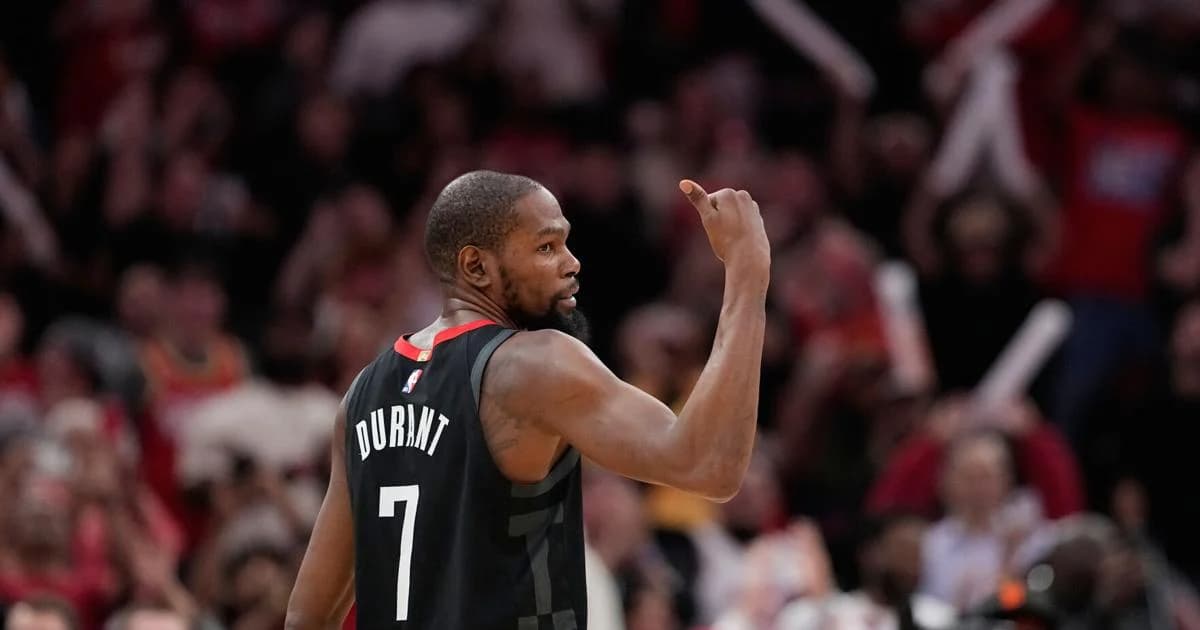 A basketball player wearing a Houston jersey raises his arm toward the crowd during a game.