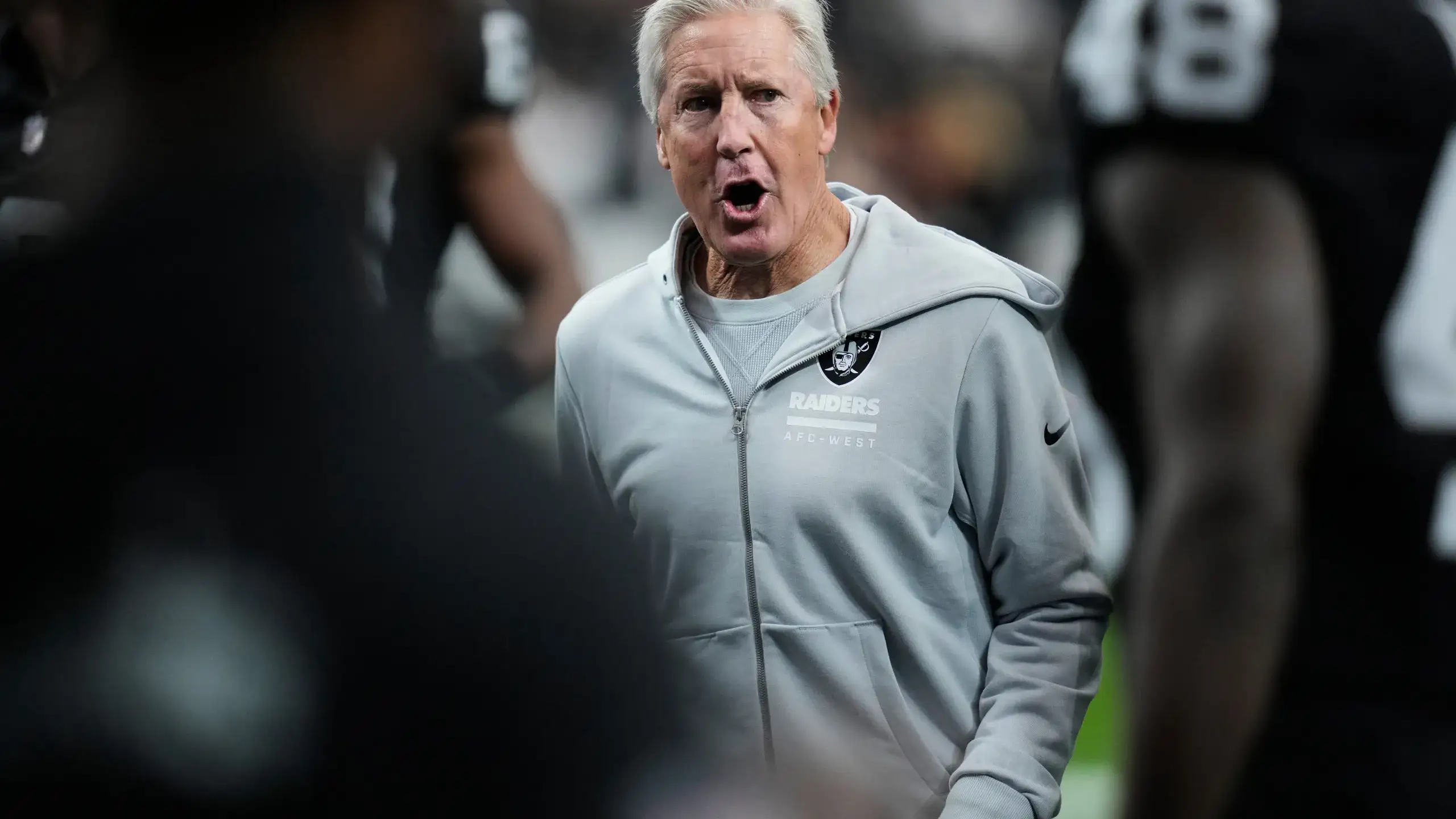 A Raiders coach shouts instructions to players on the sideline during a game.