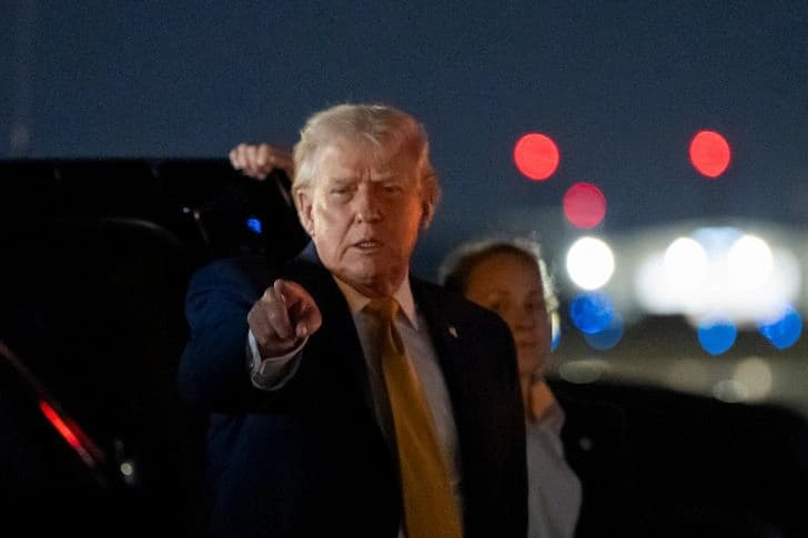President Donald Trump gestures while arriving at an airport at night accompanied by aides