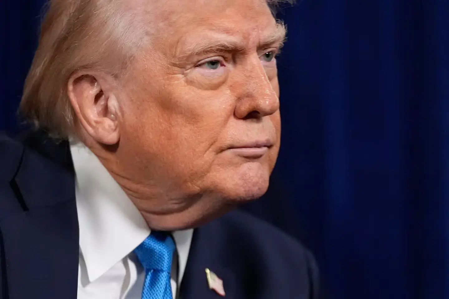 A U.S. president listens during a formal event, shown in close-up against a dark background.