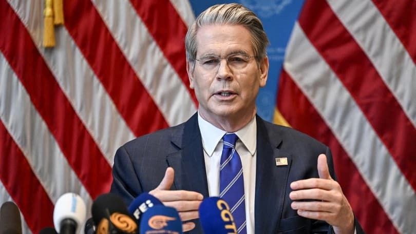 Politician addressing media with American flags in the background.
